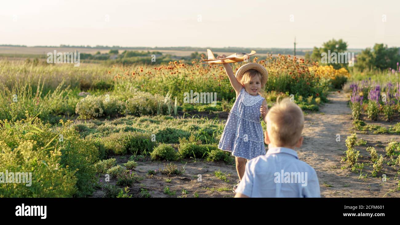childhood, provence style concept - banner 3 year old blonde little girl kid in blue dress and straw hat slavic appearance run along path with toy Stock Photo