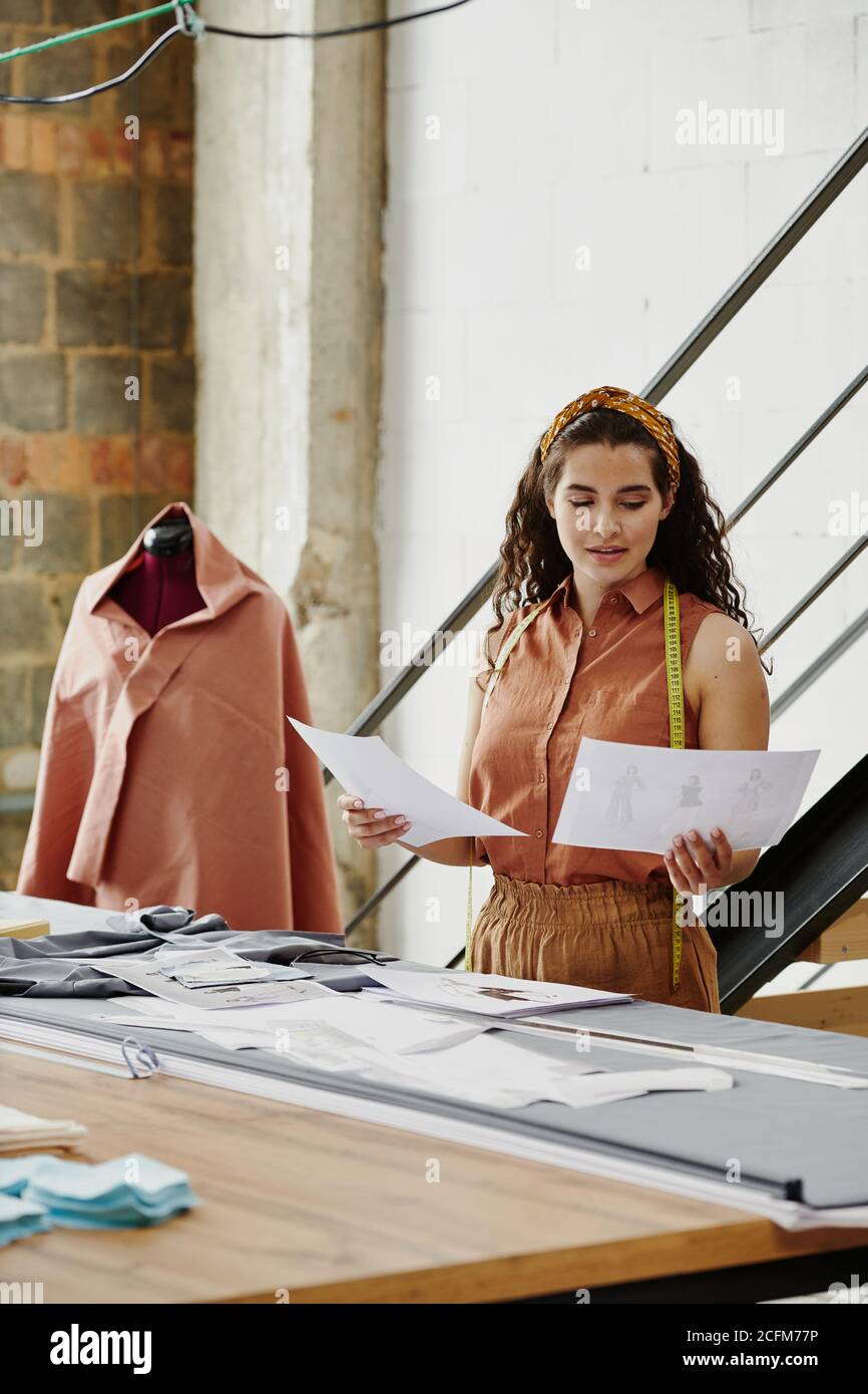 Young female designer of clothes looking through sketches of new models ...
