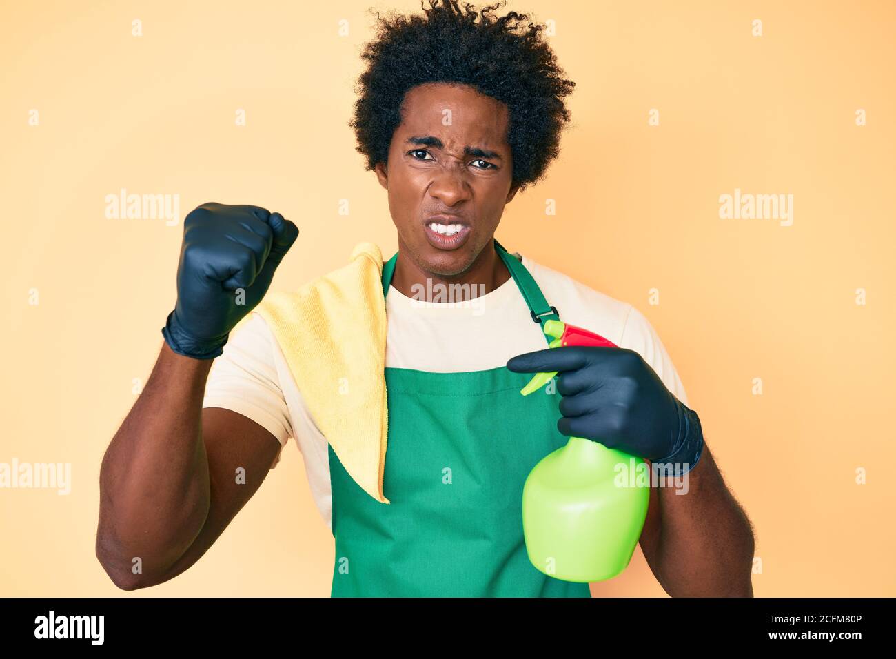 Handsome african american man with afro hair wearing apron holding cleaning spray annoyed and frustrated shouting with anger, yelling crazy with anger Stock Photo