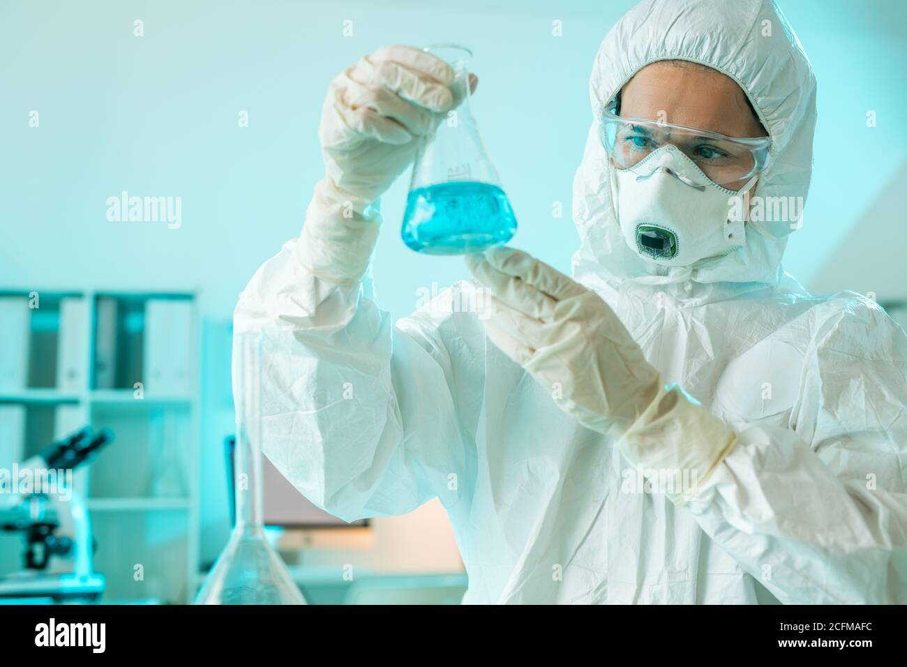 Contemporary researcher in protective coveralls studying blue liquid substance Stock Photo