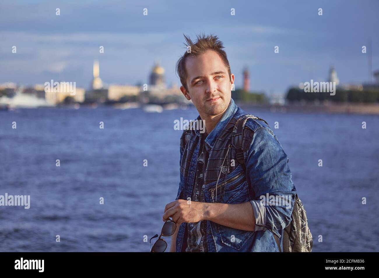 Portrait of young man on the background of the river in european city. Caucasian male tourist 27 years old is travelling in Europe. Stock Photo