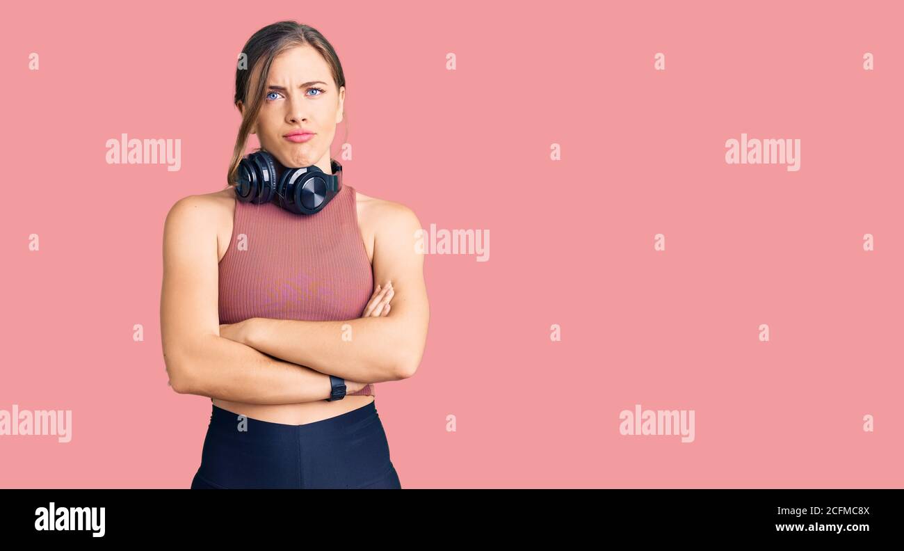 Beautiful caucasian young woman wearing gym clothes and using headphones skeptic and nervous, disapproving expression on face with crossed arms. negat Stock Photo