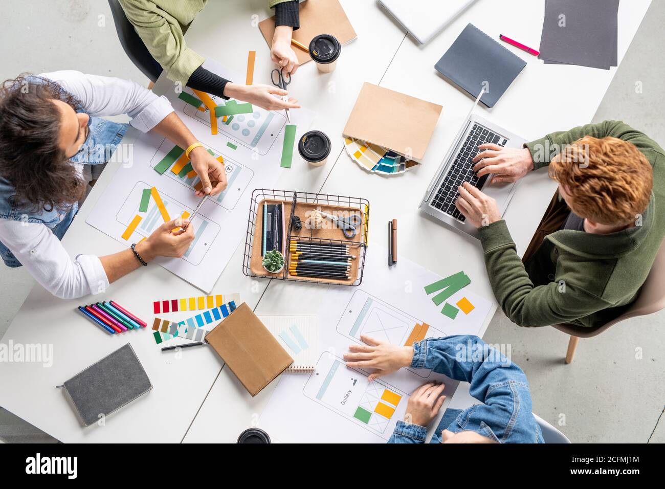 View of four contemporary designers of new mobile applications sitting by table Stock Photo