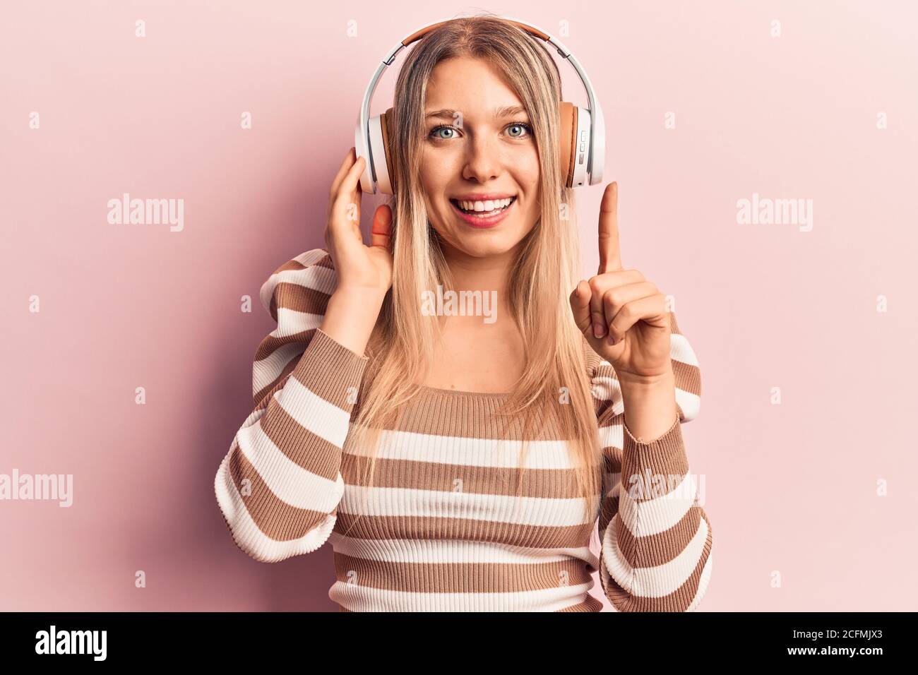 Young blonde woman listening to music using headphones smiling with an ...