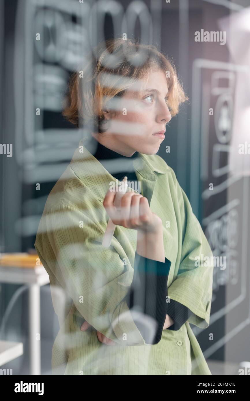 Young pensive female mobile application developer concentrating on work Stock Photo