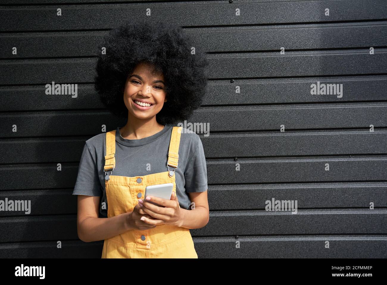 Happy African young hipster woman with Afro hair using smartphone, portrait. Stock Photo