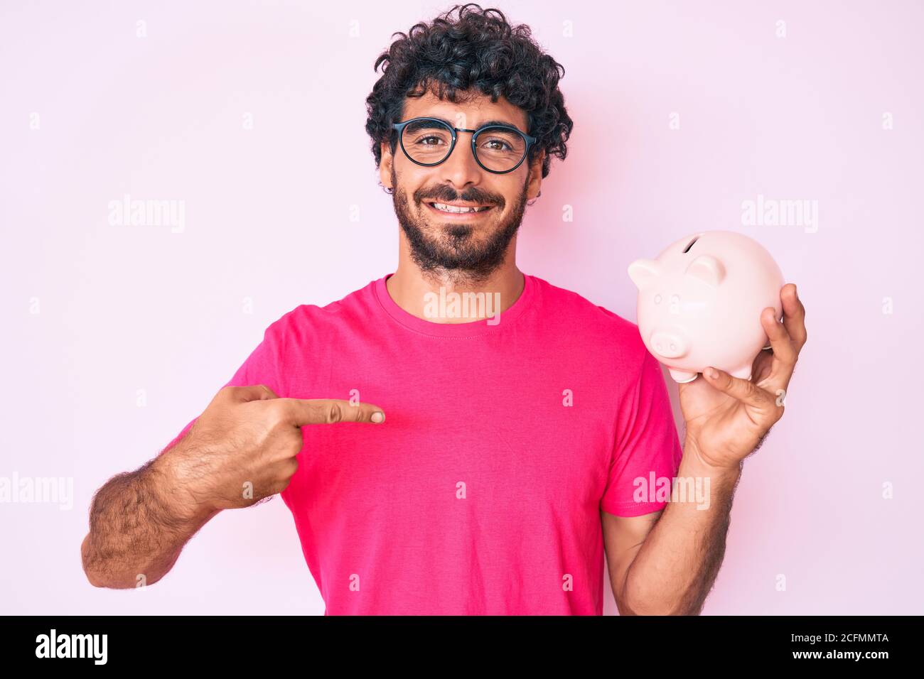 Handsome young man with curly hair and bear holding piggy bank pointing ...