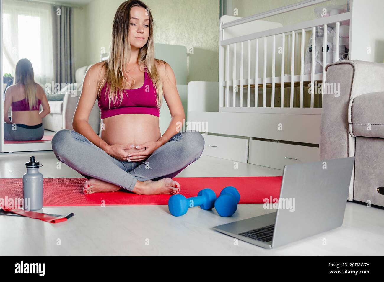 portrait of young beautiful caucasian pregnant woman sitting on yoga mat watching workout tutorial at home, copy space. Healthy pregnancy. Stock Photo
