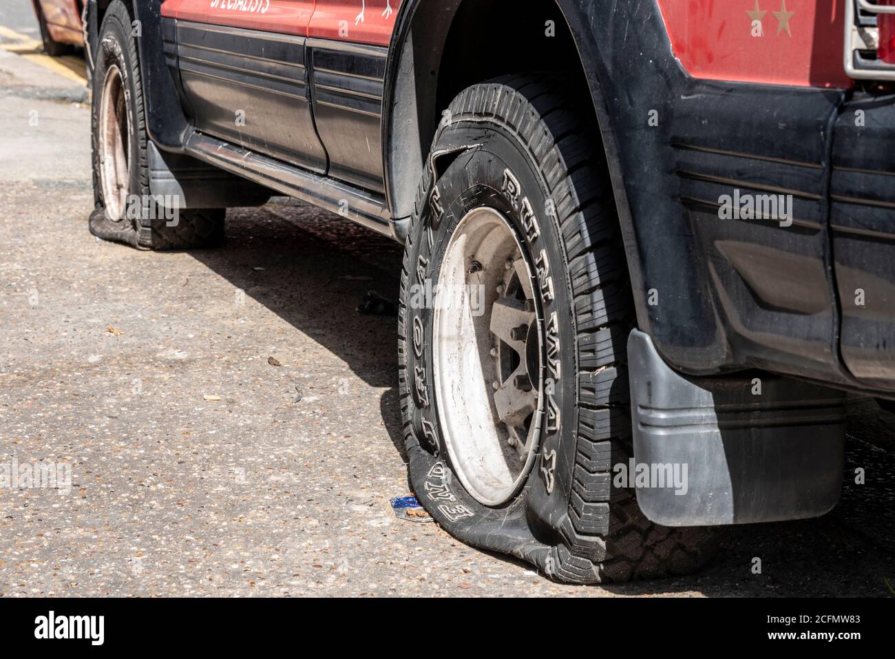 Slashed car tyres on a 4x4 vehicle. Expensive tires vandalised on car. Chunky all terrain tyres slashed in street. Authentic criminal action on road Stock Photo