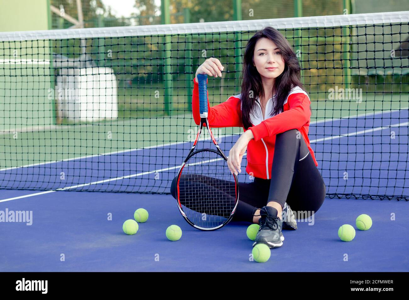 Young pretty woman sitting leaning on tennis net, resting relaxing after training. Portrait of sportswoman on tennis blue court. Healthy life. Stock Photo