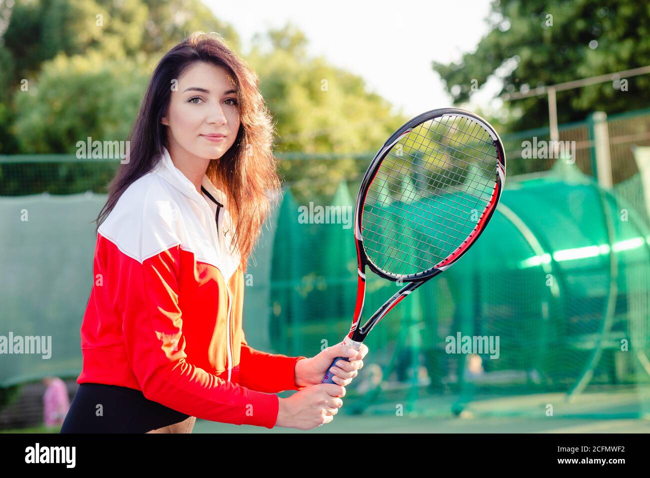 Portrait of a beautiful young female tennis player in sports clothing holding tennis racket on court. Stock Photo