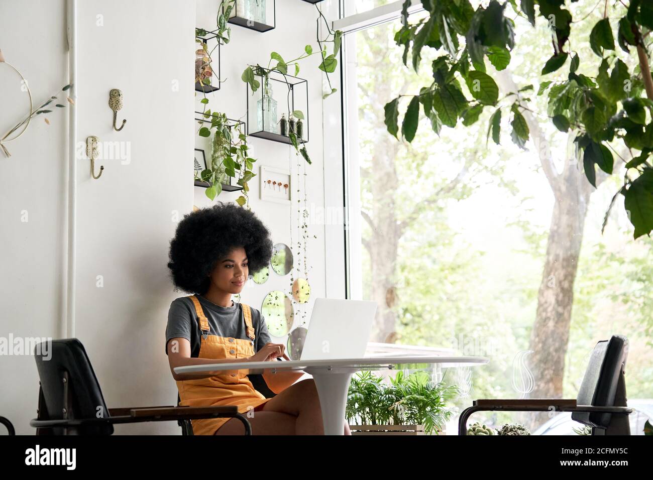 Happy African woman student using laptop sitting at table at home, in cafe. Stock Photo