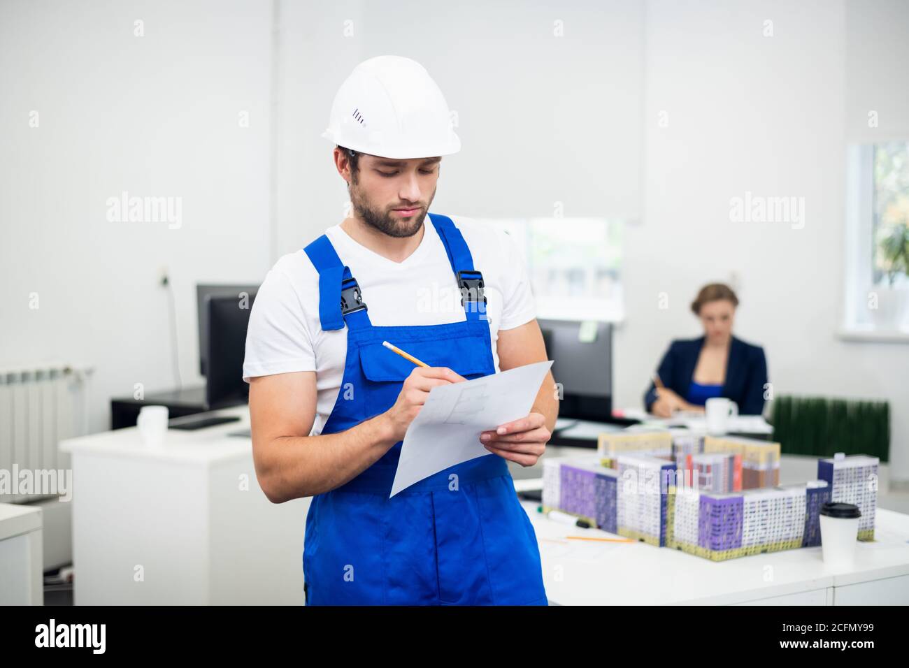 Young construction supervisor in a white helmet taking notes while in office. Stock Photo