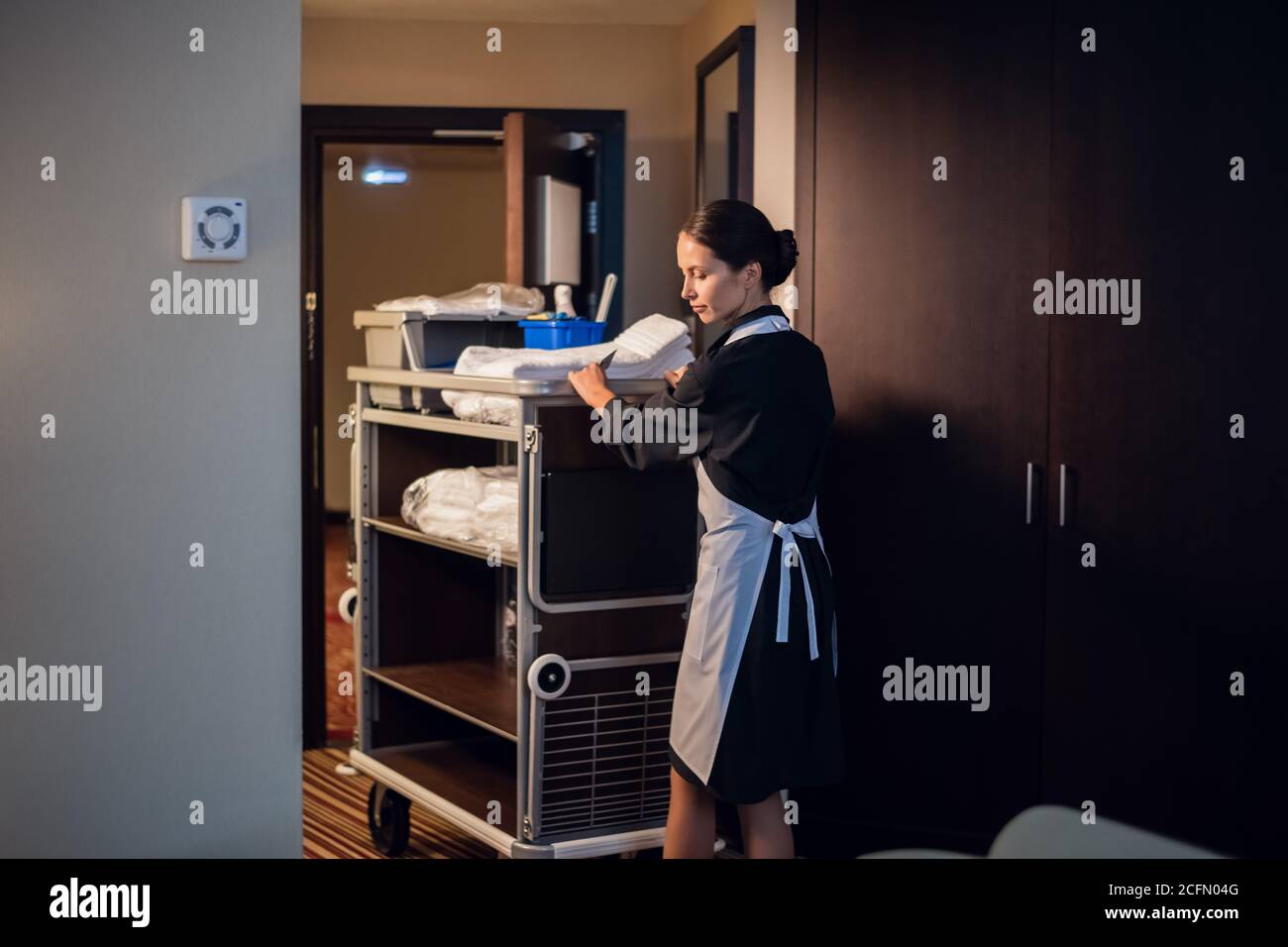 A housekeeping lady in a uniform entering a room with a trolley Stock
