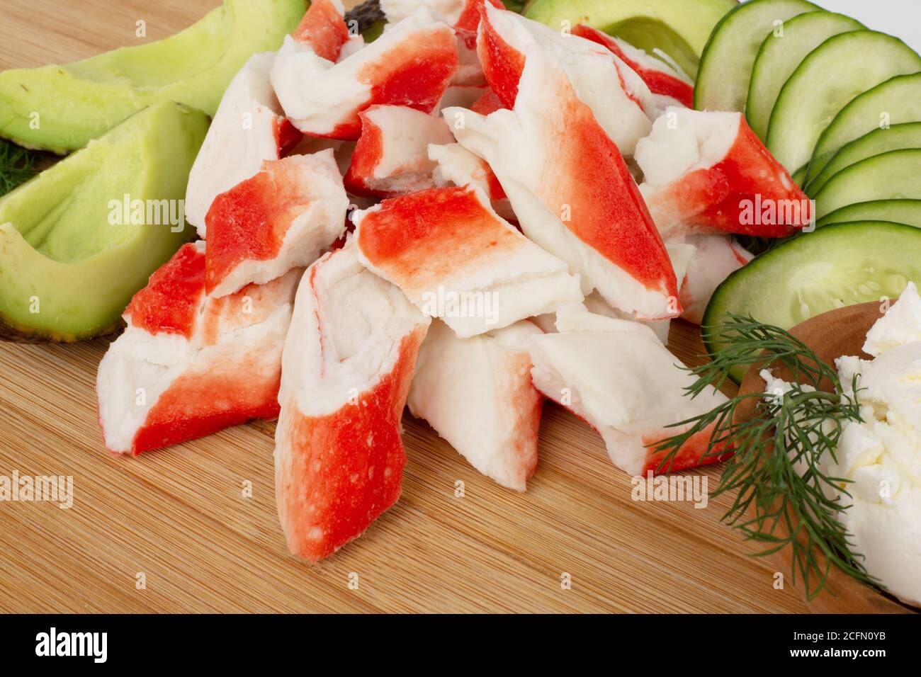 Crab sticks cut meat and vegetables avocado cut cucumbers on wooden cutting board close up Stock Photo