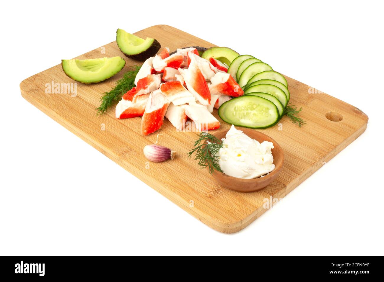 Crab sticks cut meat and vegetables avocado cut cucumbers on wooden cutting board isolated on white background Stock Photo