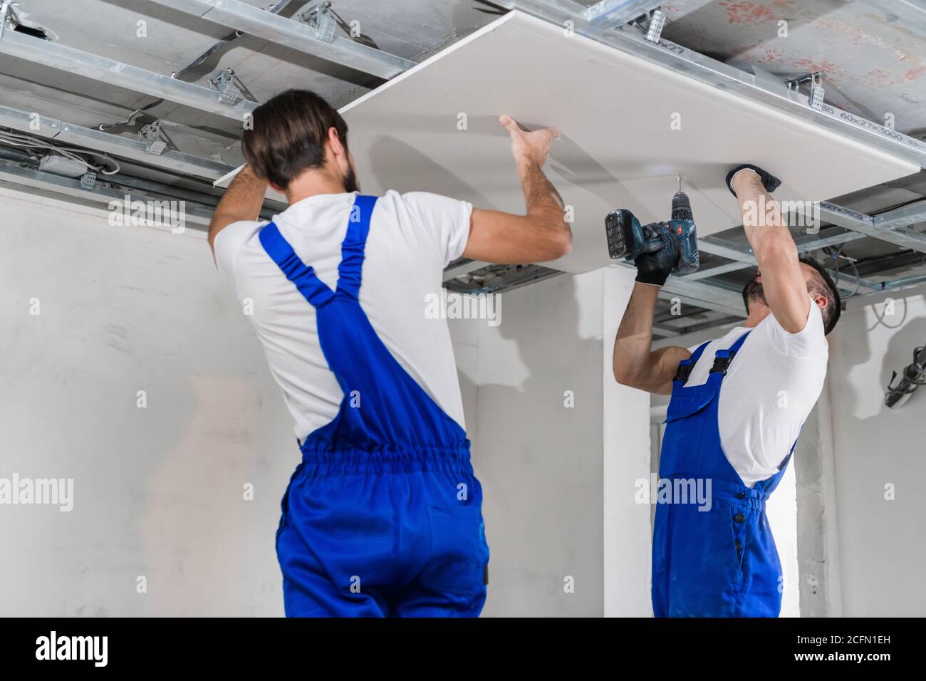 Workers in blue overalls stand on a ladder and make a ceiling Stock Photo