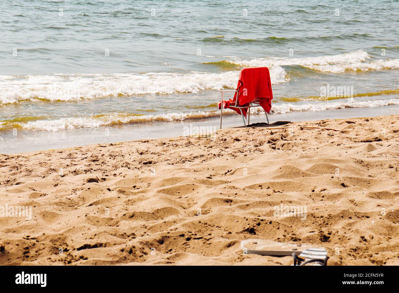 Seascape beach scene: white empty chair with red towel standing by the sea on sunny summer day. Stock Photo
