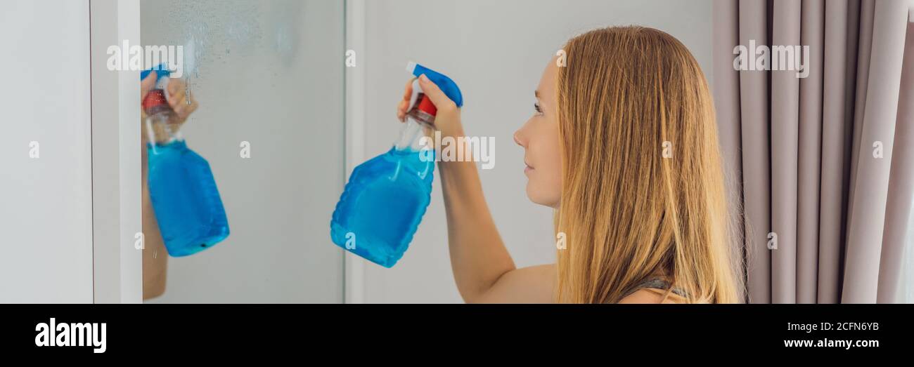 Young beautiful woman cleaning mirror. Cleaning service. Maid cleaning at home BANNER, LONG FORMAT Stock Photo