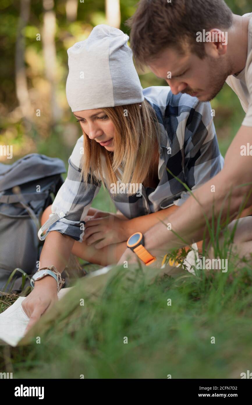 Young hikers sitting on the ground looking at an old map with a compass. Hiking couple in nature. Stock Photo