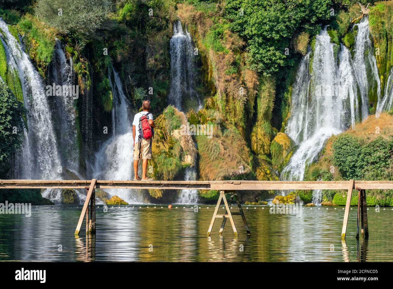 Unidentified tourist stands on the wooden bridge in front of beautiful Kravica waterfall in Bosnia and Herzegovina Stock Photo