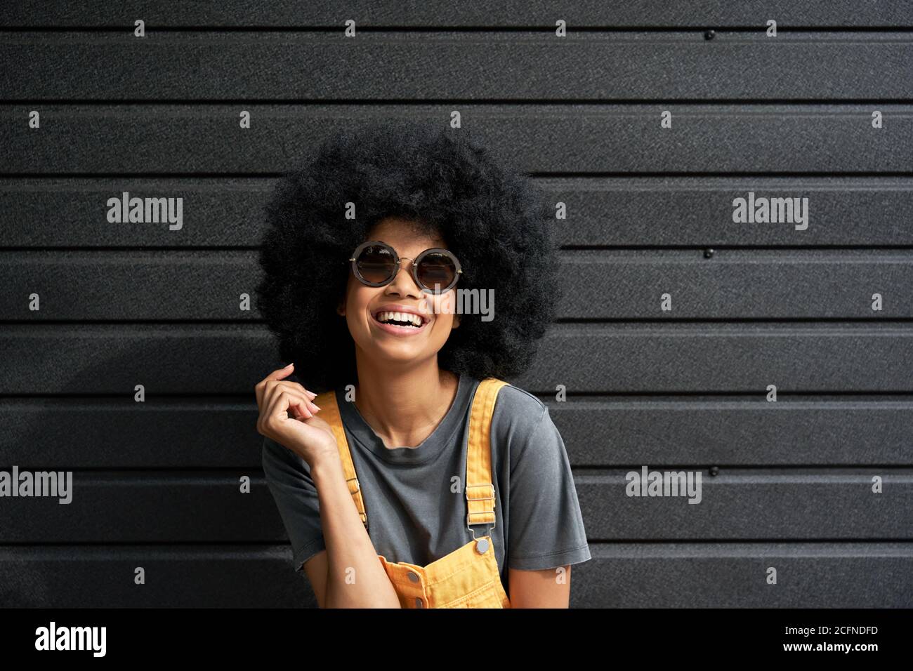 Happy funny African hipster woman wear stylish sunglasses against black wall. Stock Photo
