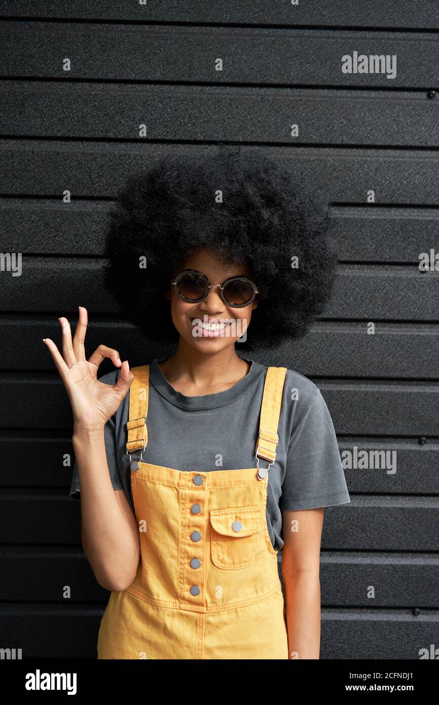 Happy African hipster lady wear stylish glasses stand against black wall. Stock Photo