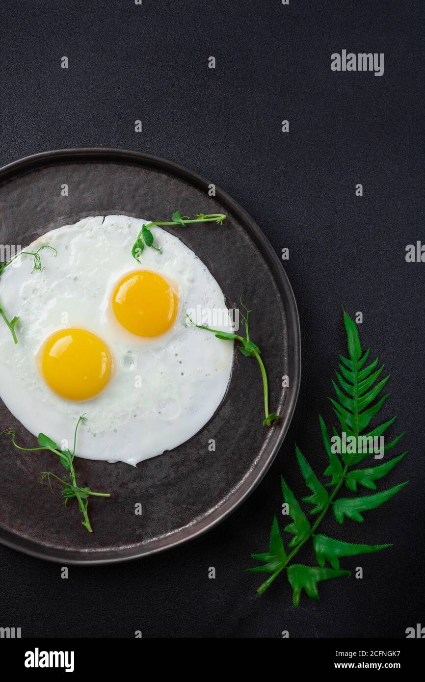 Breakfast with two fried eggs and herbs on black background Stock Photo
