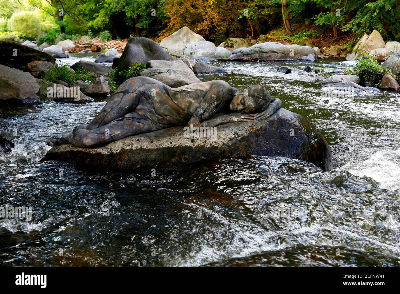 Nature Art: Stone in the river bodypainting and photoshooting with model Daniela on a stone in the Chemnitz river in Schweizerthal on September 6, 2020 - Bodypainting artist: Joerg Duesterwald Stock Photo