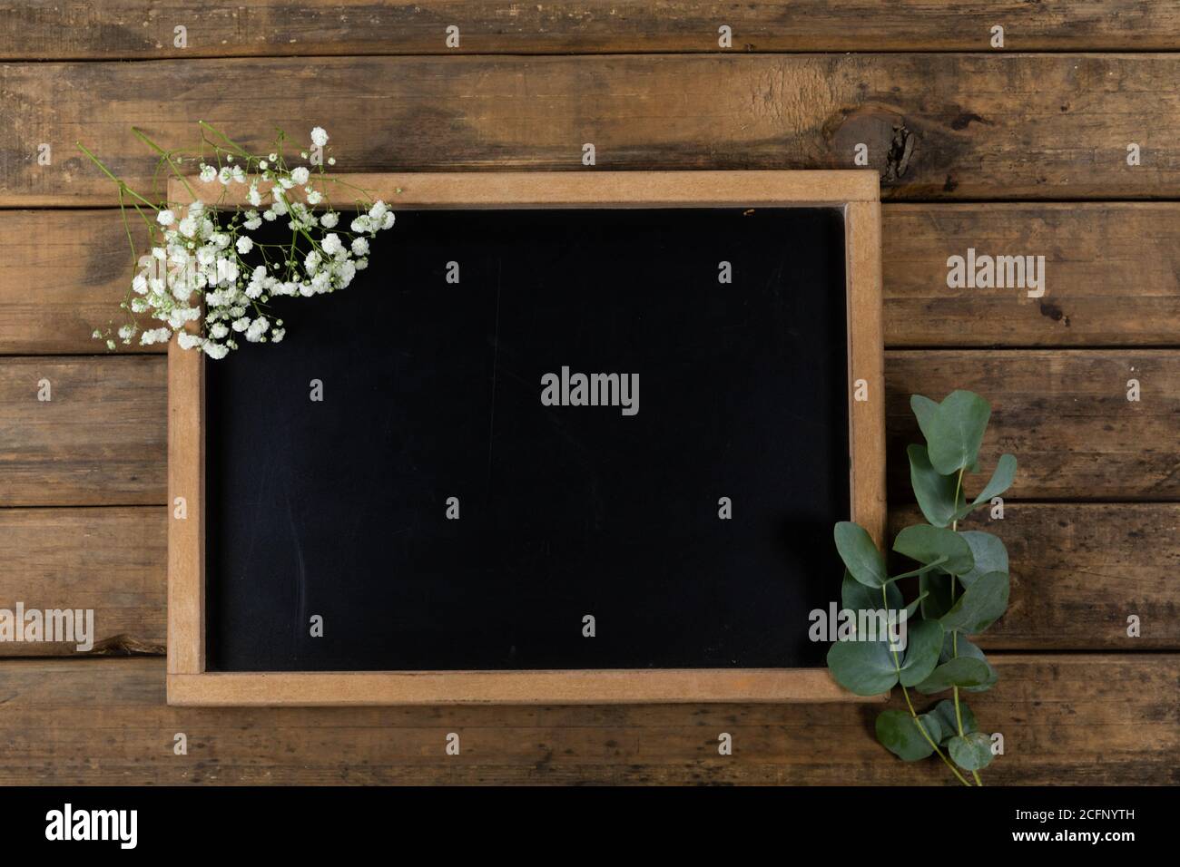 View of a black board surrounded by flowers on wood table background Stock Photo