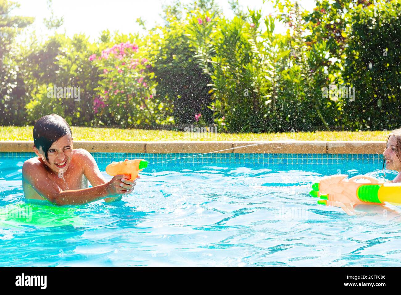 Boy in swimming pool shooting with water squirt gun on sunny summer day
