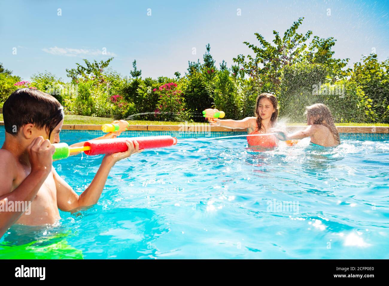 Kids play in swimming pool shooting with watergun squirt pistol on