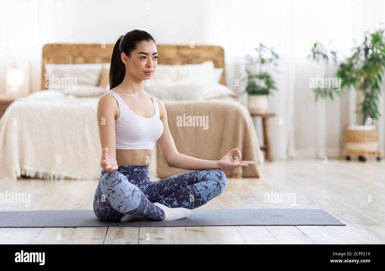 Life Balance. Asian Girl Practicing Yoga At Home, Meditating In Lotus Position Stock Photo