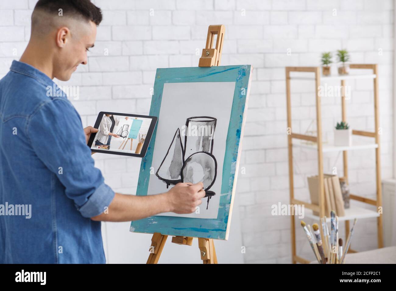 Drawing lesson remotely. Happy guy draws picture and looks at tablet