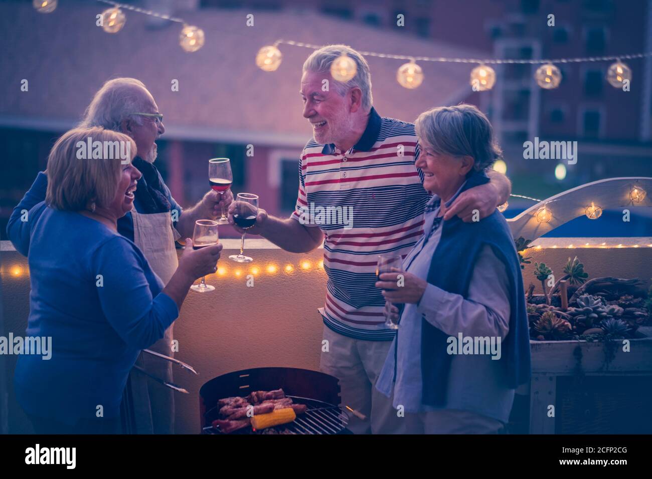 Group of cheerful and happy senior friends people clinking and enjoying together the dinner outdoor in terrace at home with city view - people togethe Stock Photo