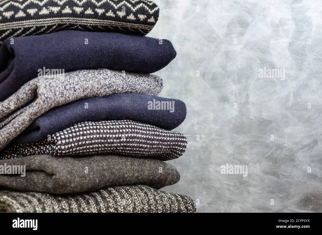 Stack of folded warm knitted men's sweaters on gray background. Copy space. Closeup Stock Photo
