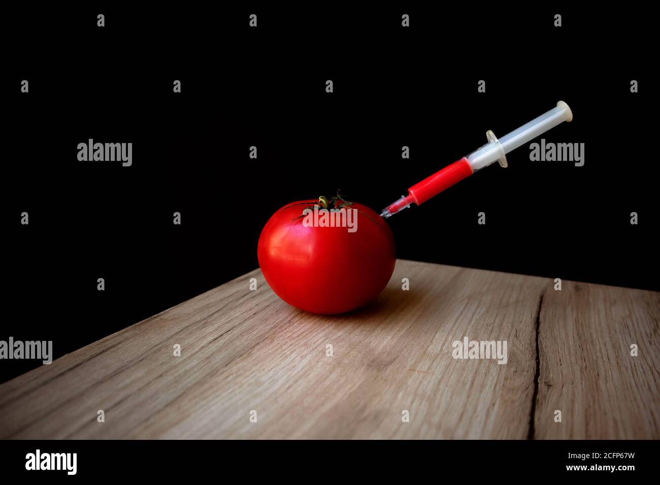 Ripe red tomato on a wooden board and syringe inside it extracting red liquid Stock Photo