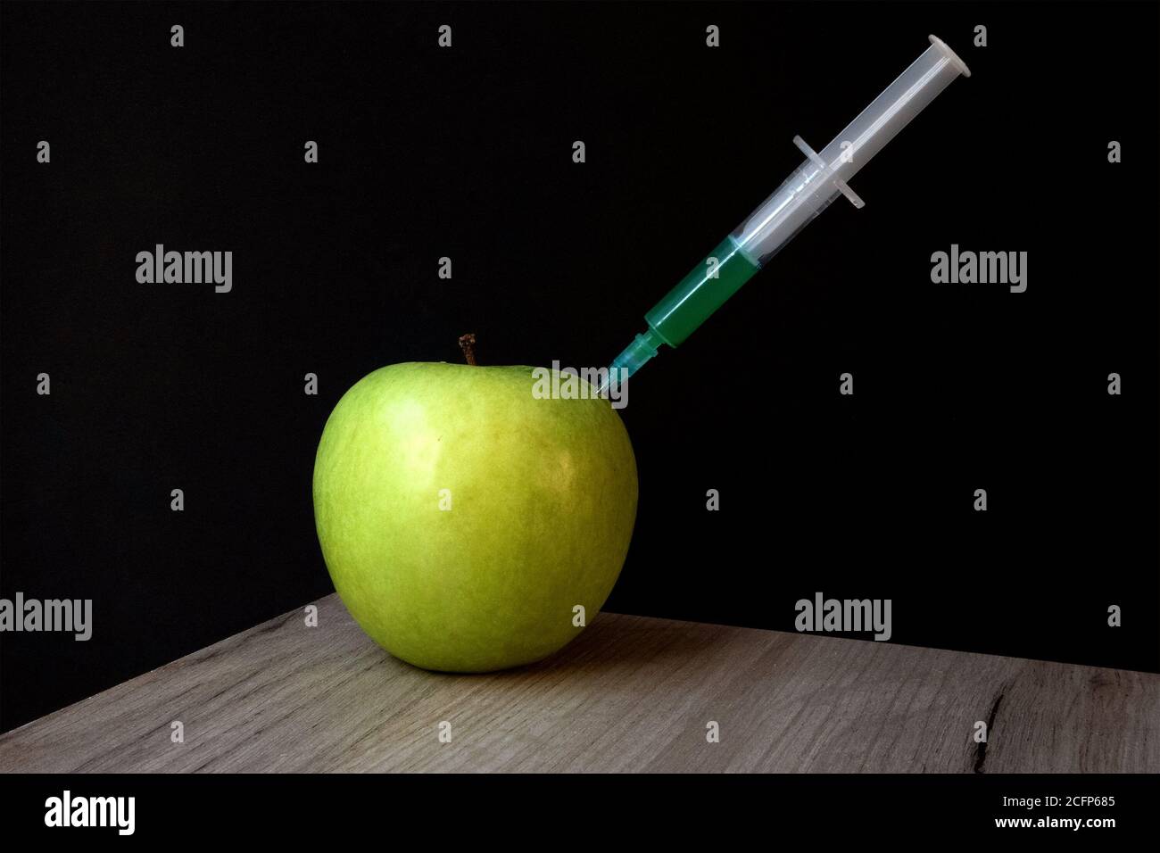 Green apple on a wooden board and syringe inside it extracting green liquid Stock Photo