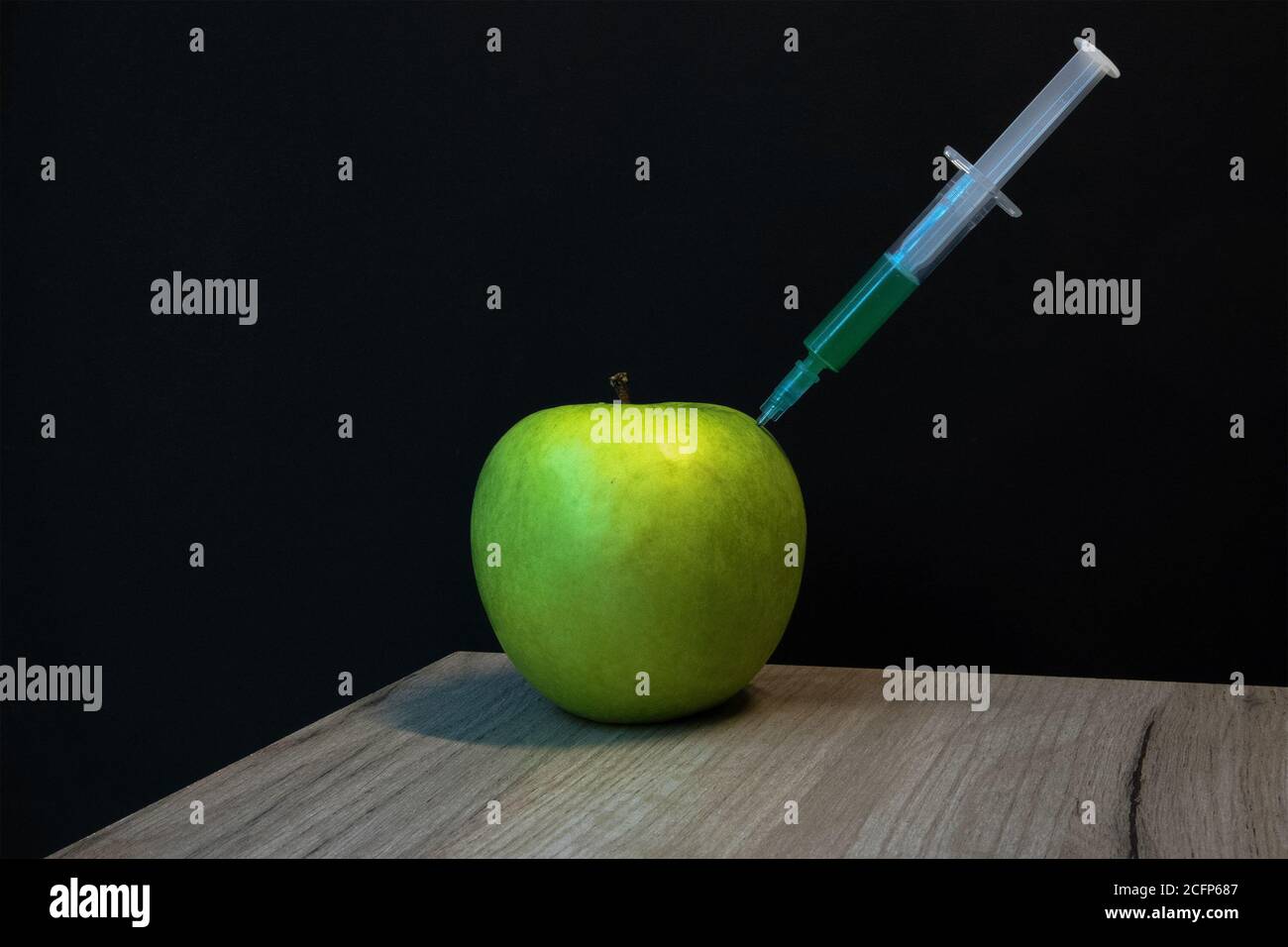 Green apple on a wooden board and syringe inside it extracting green liquid Stock Photo