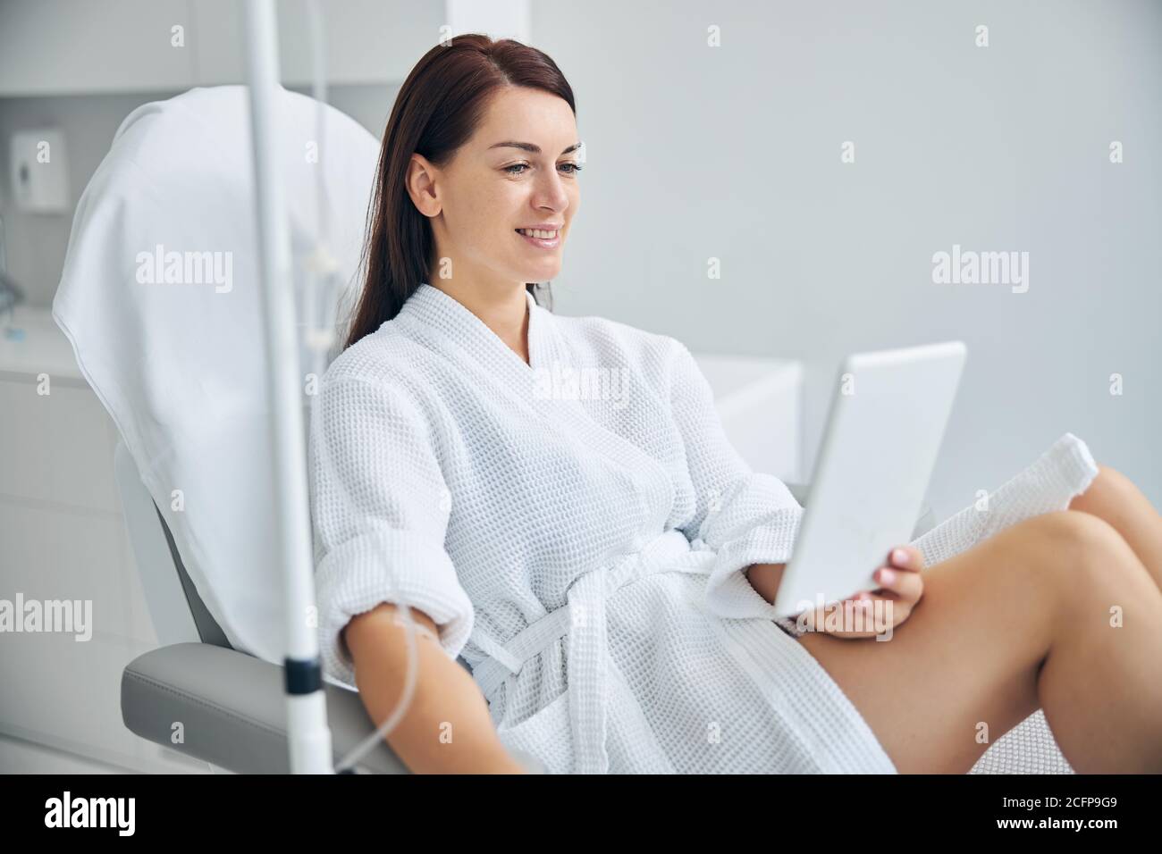 Smiling spa client using a gadget during a medical procedure Stock Photo