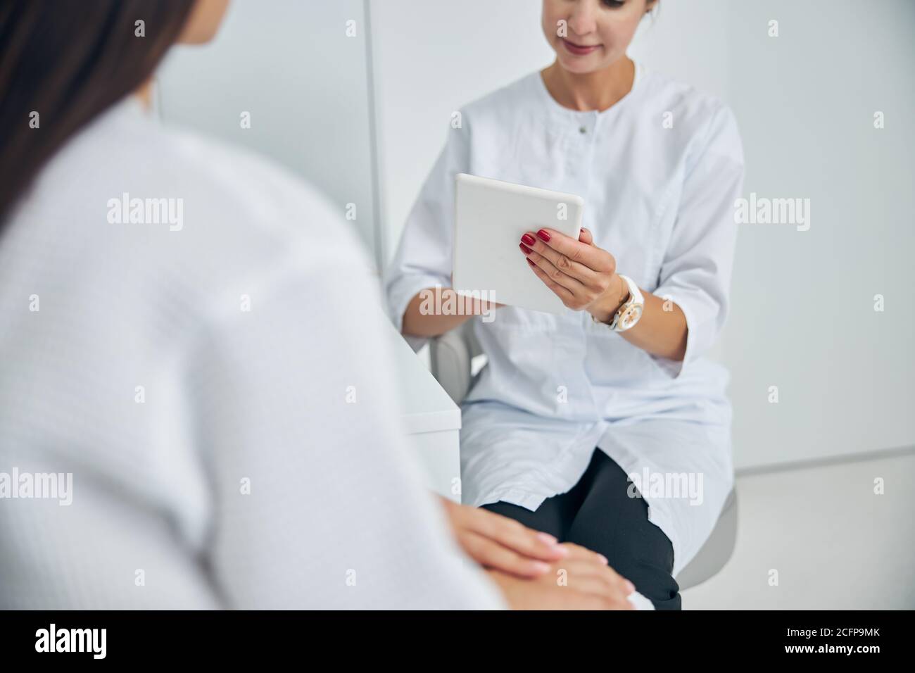 Dermatologist with a gadget sitting by her client Stock Photo