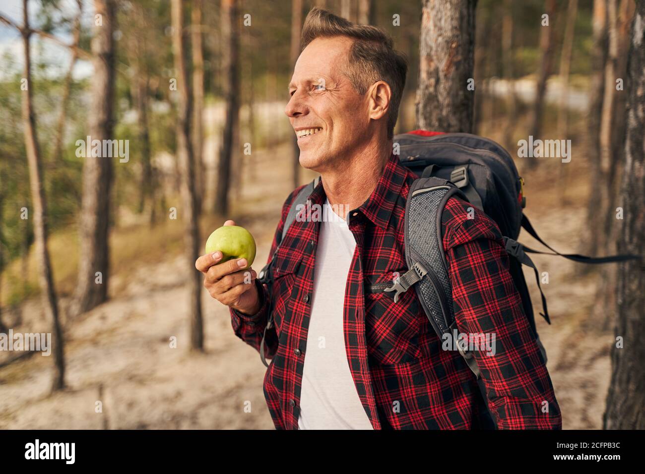 Hungry man eating apple while hiking in wood Stock Photo