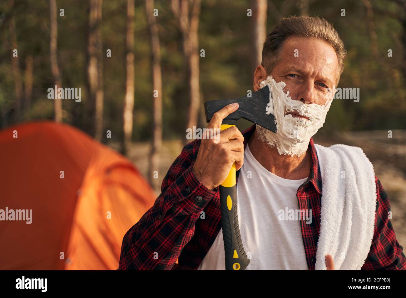 Mature man shaving with axe while going camping Stock Photo
