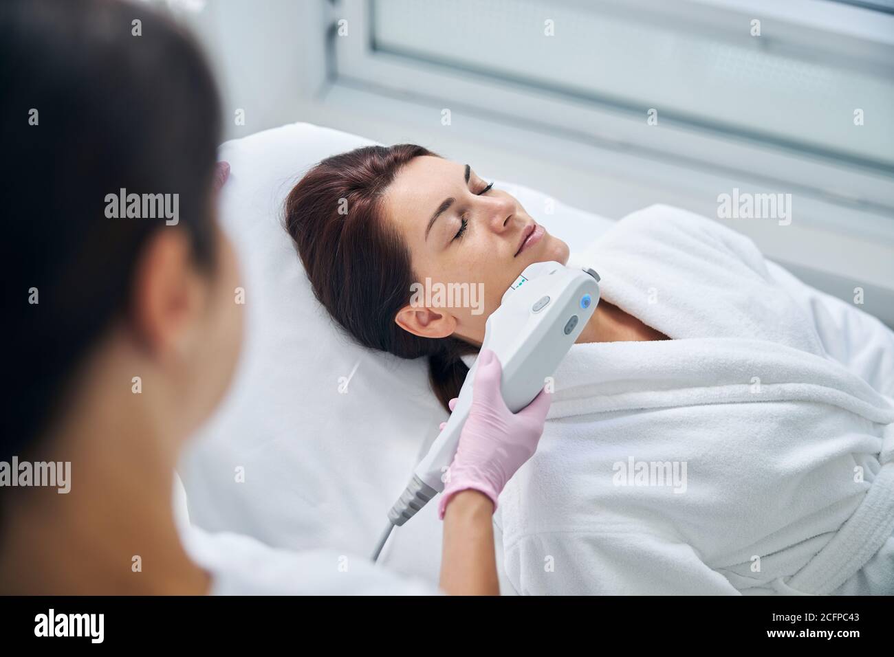 Qualified dermatologist performing an ultrasound facial treatment Stock