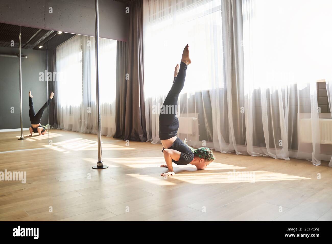 Beautiful charming female doing acrobatic element on the wooden floor in dance studio Stock Photo