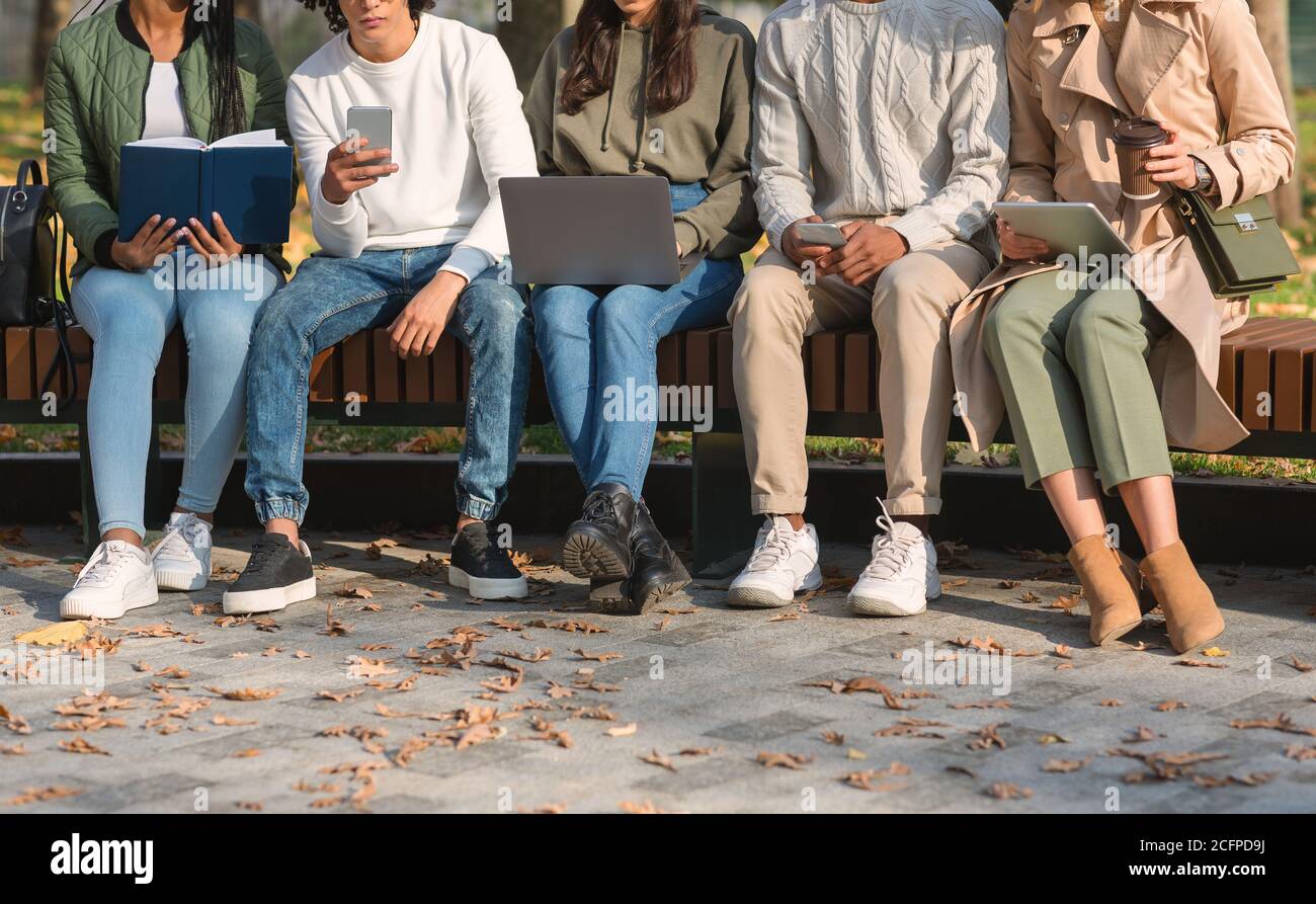 Friends spending time in park, studying, using cellphones Stock Photo