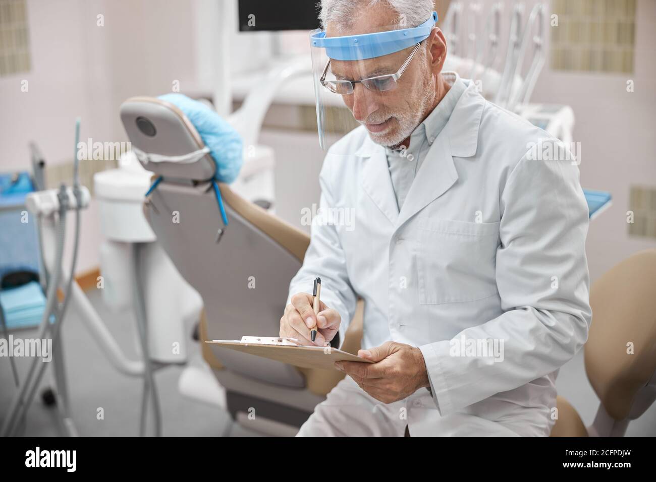 Busy dentist taking notes while sitting in his office Stock Photo