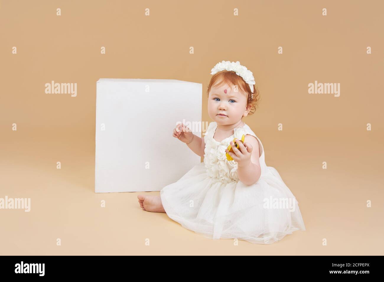 Little red-haired baby girl is playing on a beige background. Big mole on the forehead, not like everyone else Stock Photo