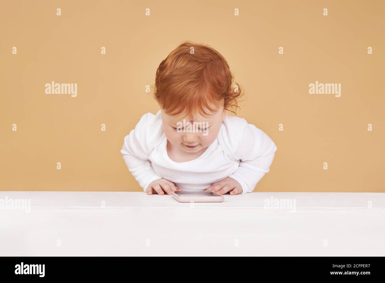 Little red-haired baby girl is playing on a beige background. Big mole on the forehead, not like everyone else Stock Photo