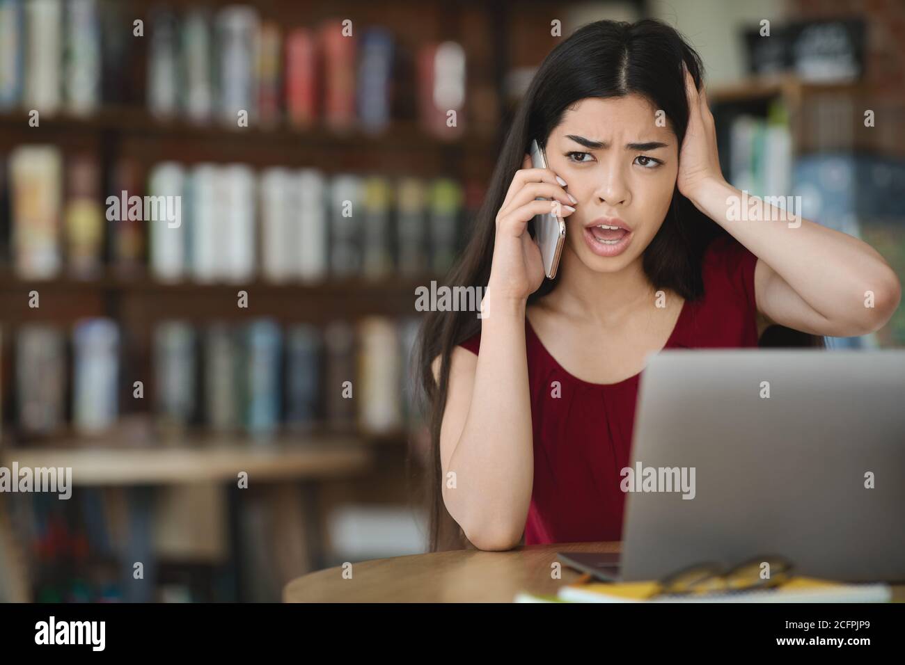 Frustrated asian woman having computer problems, talking on cellphone with customer support Stock Photo